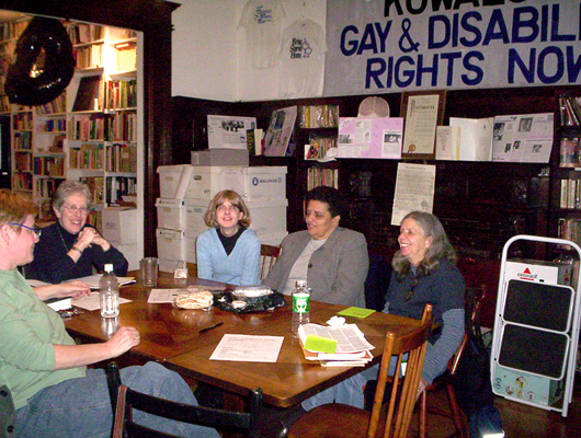 Five Lesbians sitting around a table inside the Lesbian Herstory Archives. They are smiling and engaged in conversation.