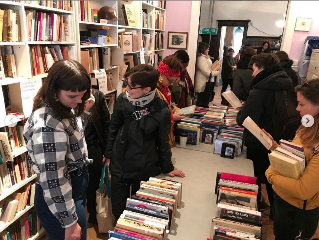 Visitors look through books displayed along both sides of a row of tables. Shelves full of books line the room.