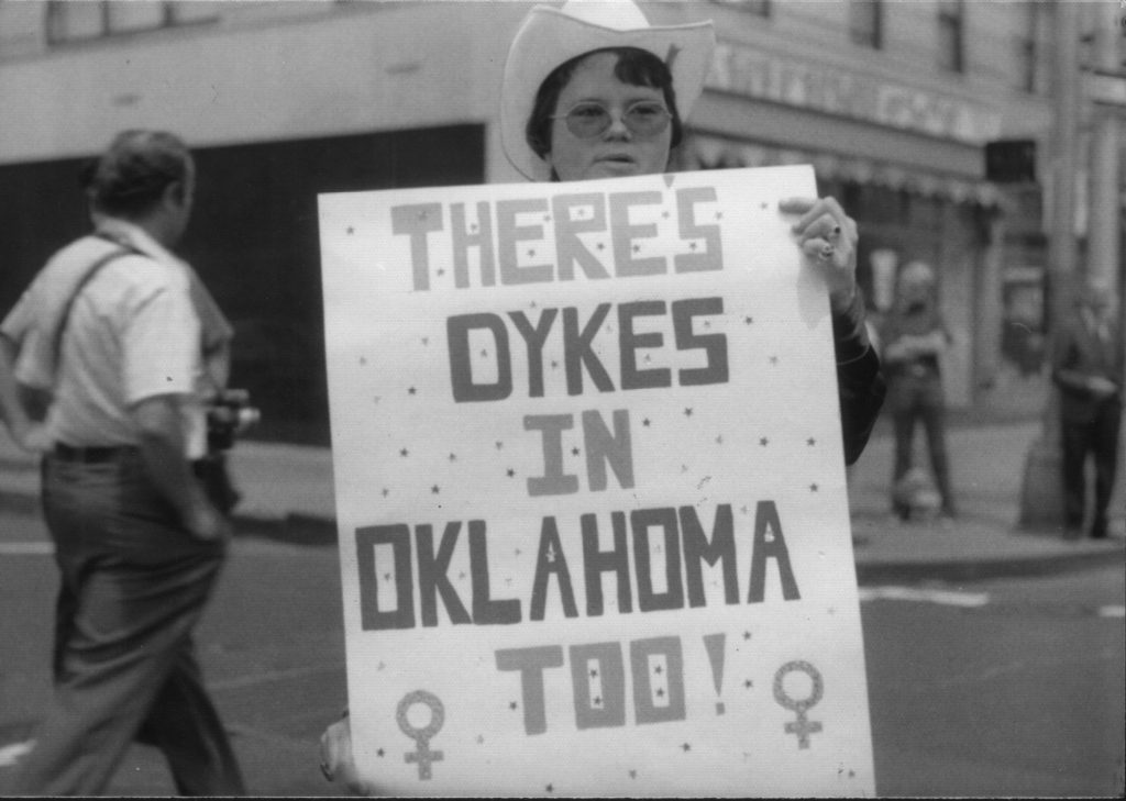 A Lesbian holding a large sign that reads "There's Dykes in Oklahoma Too!" 