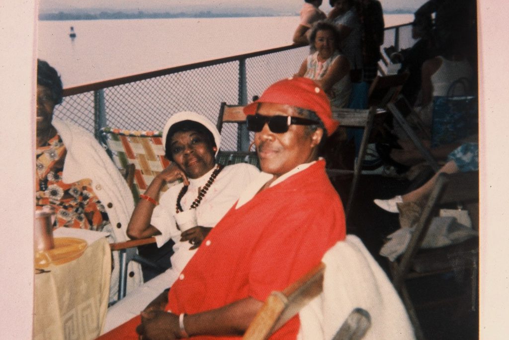 Two Black Lesbians sitting in chairs on a boat deck. They are smiling and appear to be in relaxed postures.