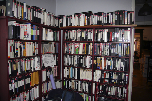 Tall shelves filled with VHS tapes in the corner of a room.